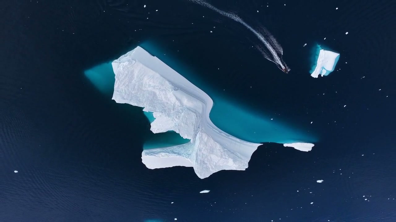 A Zodiac heads down through open water beside an iceberg, with its wake curving behind it